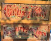 Photo showing two wooden framed cross stitch pieces featuring text and floral motifs, with natural light casting shadows. One frame glass cracked but kept original with glue.