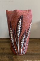Front view of reddish ceramic vase with raised wheat stalk decoration, showing texture and glaze condition.