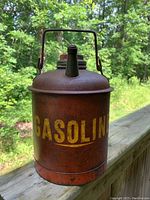 Front view of the red metal gas can with yellow painted 'GASOLIN' text and rusted surface.