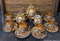 Full view of all tea set pieces grouped together on dark surface in front of wooden background.