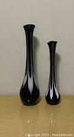 Front view showing both tall black glass Murano vases with white pattern on tan surface.