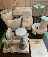 Overview of Braun Kitchen Machine KM 32 with attachments and recipe book showing main mixing bowl, blender jar, and various attachments.