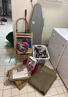 View of stepladder, wood chair, cleaning supplies, ironing board, buckets, small carpet, laundry basket with hangers