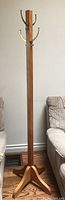 Full view of wooden coat rack positioned between two couches on hardwood floor.