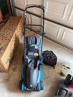 Front view of Yardworks electric lawn mower with extension cord placed nearby on garage floor.
