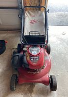 Front-facing view of the Craftsman mower showing the red steel deck, engine housing and attached canvas bag under folded handle