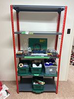Full front view of red and gray metal shelf holding various craft supplies and bins. Shows structure and shelving levels.