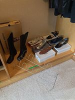 Wide view showing black boots, assorted women's shoes, metal shoe rack in front