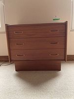 Front view of teak dresser showing three drawers and plinth base