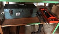 Blue metal toolbox with handle on wooden shelf with orange metal tray containing tools beside it