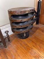 Side view of the large antique wooden pulley block showing the circular wooden frame and metal pulleys inside.