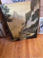 Asian-style landscape painting on canvas leaning against cardboard box.