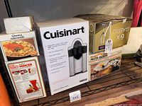 Full view of boxed kitchenware including Cuisinart reamer, Lillo mincer, ravioli maker box, pasta maker box, and gold champagne flutes box.