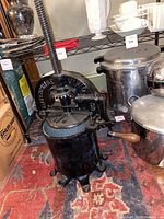 Cast iron fruit press standing on a carpeted floor near stainless steel kitchen pots.