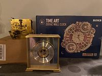 Clock mechanism, mechanical brass movement, square shape with gears and levers visible.