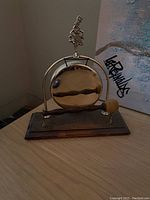 Front view of the brass gong mounted on a wooden base with mallet and decorative figure