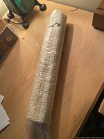 Rolled bath mat in plastic wrapping on wooden surface, showing overall item shape and packaging.