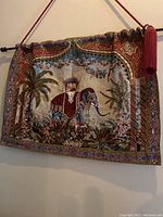 Full view of fabric wall hanging showing decorated elephant, floral and foliage motif, border, and hanging rod with tassel