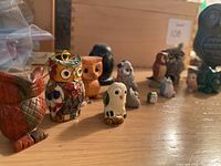 Photo showing assortment of owl figurines in various styles and sizes on wooden surface.