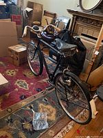 Black Raleigh bicycle viewed from rear showing full bike body and wheels inside a room with various items around.