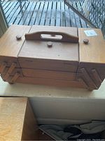 Closed wooden multi-tier sewing box with handle and knobs on top.
