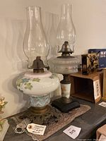 Two vintage kerosene lamps displayed on a surface, showing full view of both lamps including glass chimneys, reservoirs, and bases.