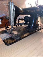 Front-left angle of black cast iron Singer sewing machine showing gold decal work and needle area