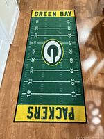 Rectangular Green Bay Packers football field-themed rug with clear yard line markings and team logos in green, yellow, and white on wooden floor.