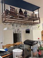 Photo showing hanging clear glass stemware glasses on metal rack above kitchen island, with popcorn maker and coffee maker on countertop.