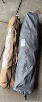 Two camping equipment items inside carrying cases on concrete floor: gray KingCamp cot bag and brown shelter bag.