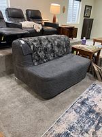 Front view of the gray convertible loveseat with a textured fabric cover and gray furry throw blanket draped on the backrest, placed on carpeted floor in a basement living space.