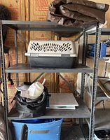 Metal shelf containing small animal crate, tarps, black bag with paint sprayer and accessories