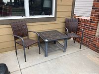 Table flanked by two woven patio chairs with metal frames, showing tiled top and shelf below