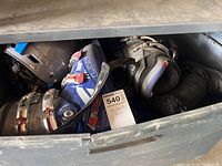 View of one blue and black Lange ski boot with adjustable buckles and grey Holt ski helmet inside a storage container.