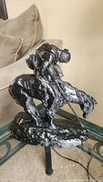 Front angle of black painted reproduction western cowboy statue on horseback, holding spear, placed on glass table.
