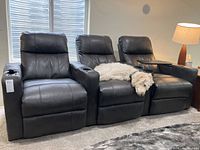 Full view of three-seat dark grey faux leather reclining theater seating with a white pet lying on the middle seat.