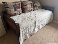 Full view of the wooden daybed made from solid wood with bedding and pillows on it in a room with carpeted floor.
