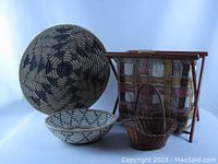 Photo showing two coiled southwest-style baskets with geometric patterns in earth tones (one large 15" diameter, one smaller 10" diameter), small dark brown rattan basket with handle, and vintage folding sewing basket with wood frame and multi-color patchwork fabric liner.