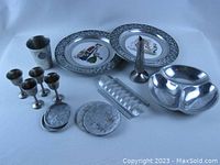 Photo showing assorted pewter and aluminum kitchen items including 4 cordial glasses, 1 pewter tumbler with Mississippi seal, 2 collector plates with pewter rims, Nambe 3-part serving bowl, toast rack, and coasters.