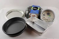 Full set of mixed baking pans showing a variety of pans including black nonstick round pans, silver aluminum pans, a fluted tart pan, and a Bundt pan still labeled.