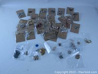 Wide view showing an assortment of bagged and carded fashion earrings and necklaces arranged on a white surface, highlighting various styles and presentations.