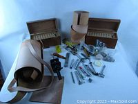 Overview photo displaying 10 leather punches and stamps, 4 wooden storage boxes with perforated inserts, bag and rolls of pigskin scraps, and assorted small leather working tools arranged on table.