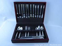 Photo showing the wood storage case open with various silverplate forks, spoons, and knives organized inside.