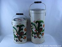 Pair of off-white metal cans with colorful handpainted Swedish folk art designs and dala horses on lids. Both have pivoting metal handles with black wooden grips. Smaller can is shorter and wider, larger can taller and slender.