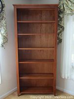 Front view of solid cherry wood tall bookcase showing five shelves and clean wood grain.