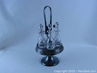 Full view of the Victorian Wilcox quadruple silver plate condiment server with six cut glass bottles displayed on a pedestal stand with central handle.