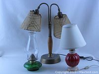 Green glass kerosene lamp, double brass electric lamp with fiberglass shades, and red painted midcentury electric lamp with white shade shown together.