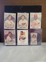 Photo showing six Topps Chrome Allen and Ginter baseball cards featuring various legendary players, each in protective sleeves or cases.