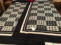 Two black and white blankets with large houndstooth pattern spread on a bed, showing full pattern and border details.