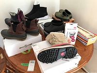 Overall view of various boots and shoes on table including brown boots, black slip-on shoes, olive green shoes, Micro O Pedi box, and colorful purse box